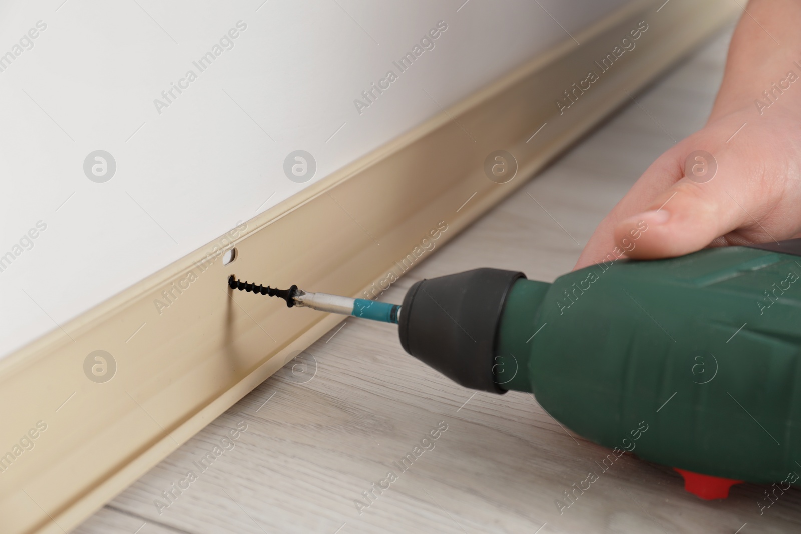 Photo of Man installing plinth on laminated floor with screwdriver in room, closeup