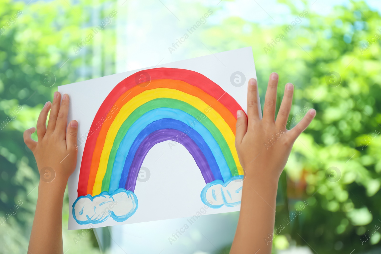 Photo of Little girl with picture of rainbow near window, closeup. Stay at home concept