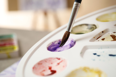 Photo of Brush and palette with watercolor paints, closeup