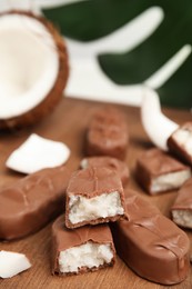 Delicious milk chocolate candy bars with coconut filling on wooden board, closeup. Space for text