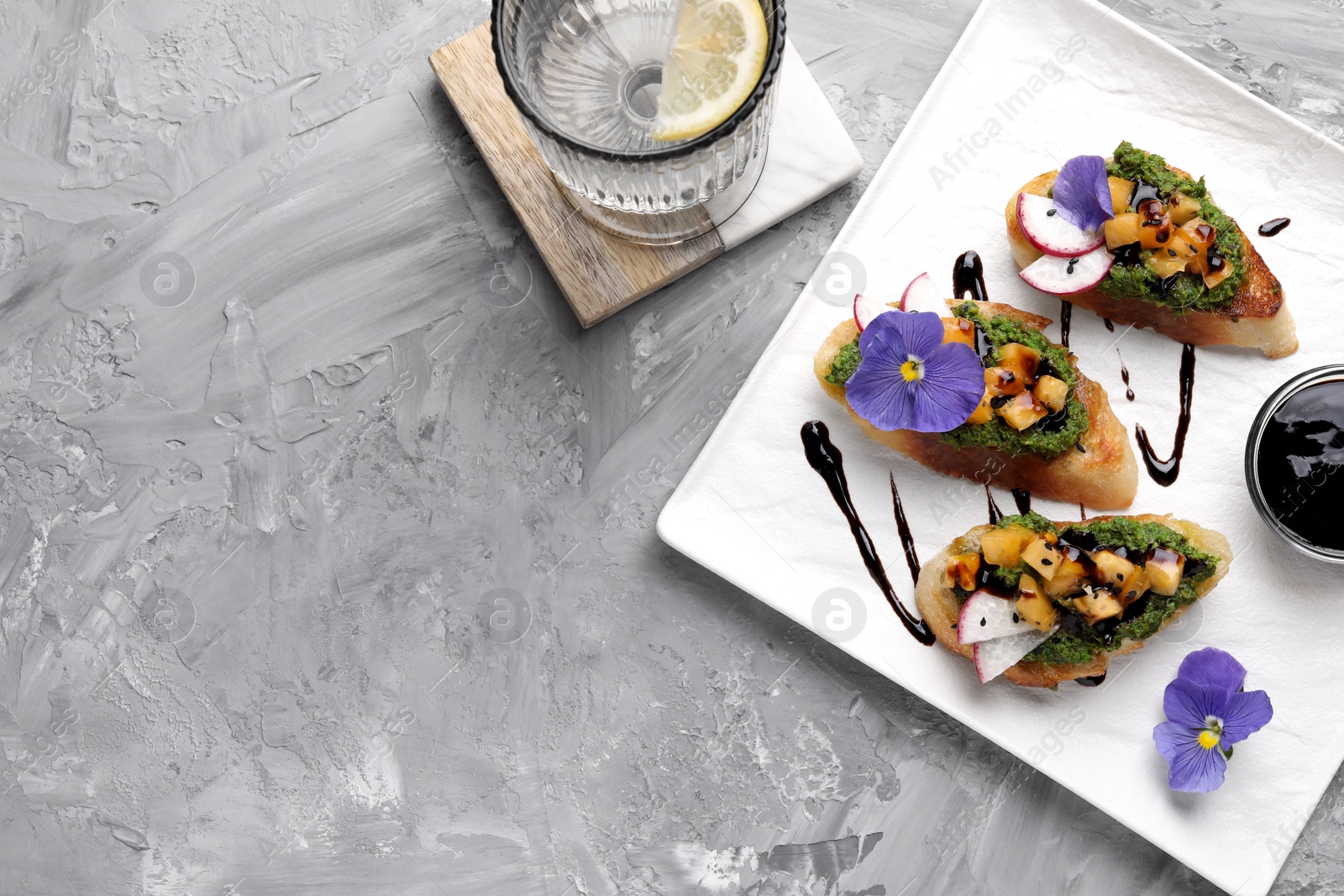 Photo of Delicious bruschettas with pesto sauce, tomatoes and balsamic vinegar served on gray textured table, flat lay. Space for text