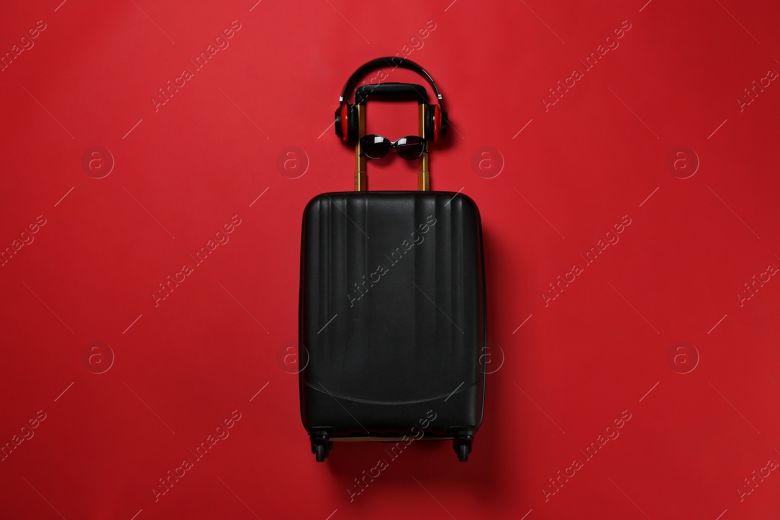 Photo of Stylish suitcase with sunglasses and headphones on color background, top view