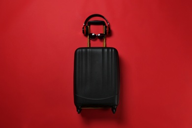 Photo of Stylish suitcase with sunglasses and headphones on color background, top view