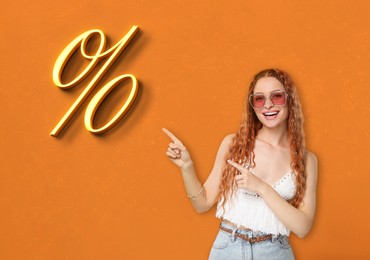 Discount offer. Happy woman pointing at percent sign on orange background