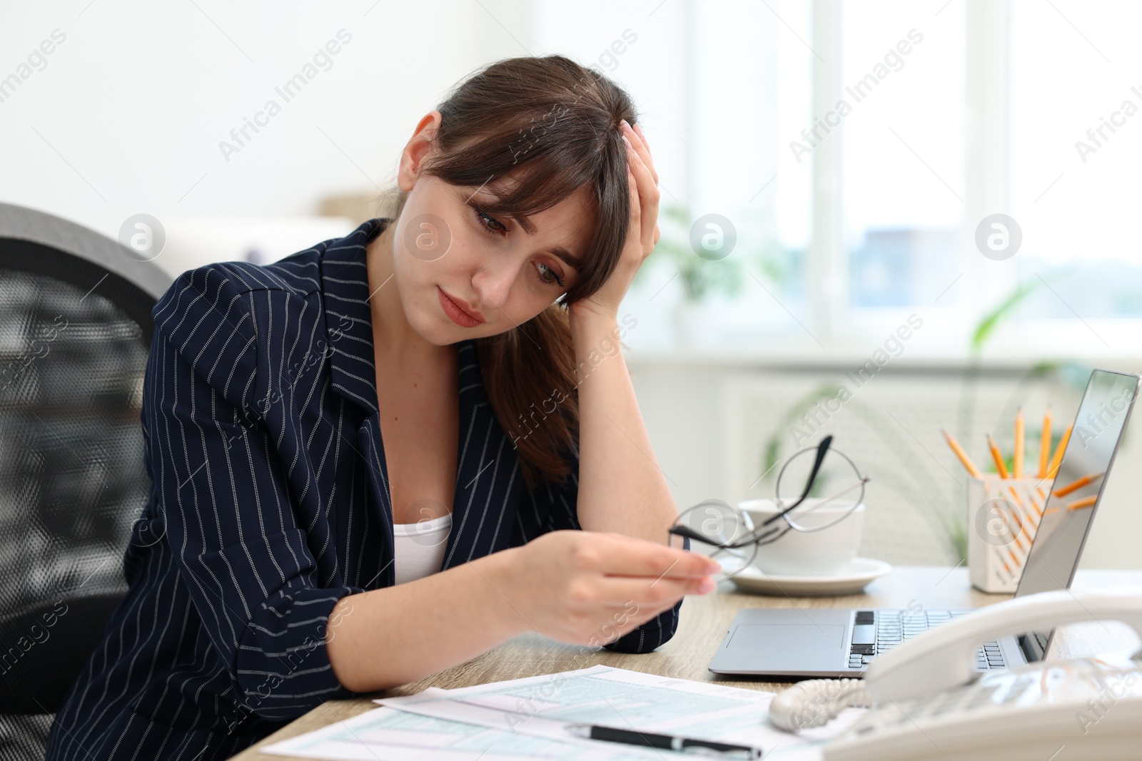 Photo of Overwhelmed office worker sitting at table with laptop and documents indoors