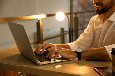 Photo of Man working with laptop at table in office, closeup