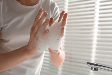 Photo of Woman washing hands with cleansing foam near sink in bathroom, closeup