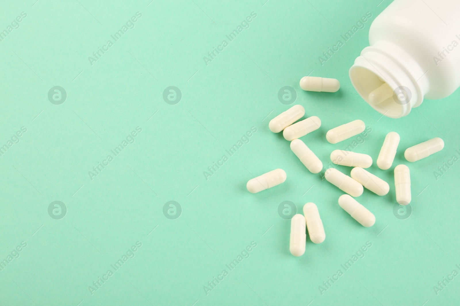 Photo of Bottle and vitamin capsules on turquoise background, above view. Space for text