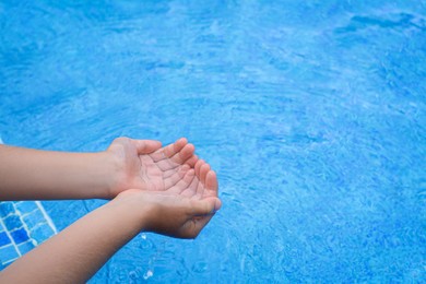 Girl holding water in hands above pool, closeup