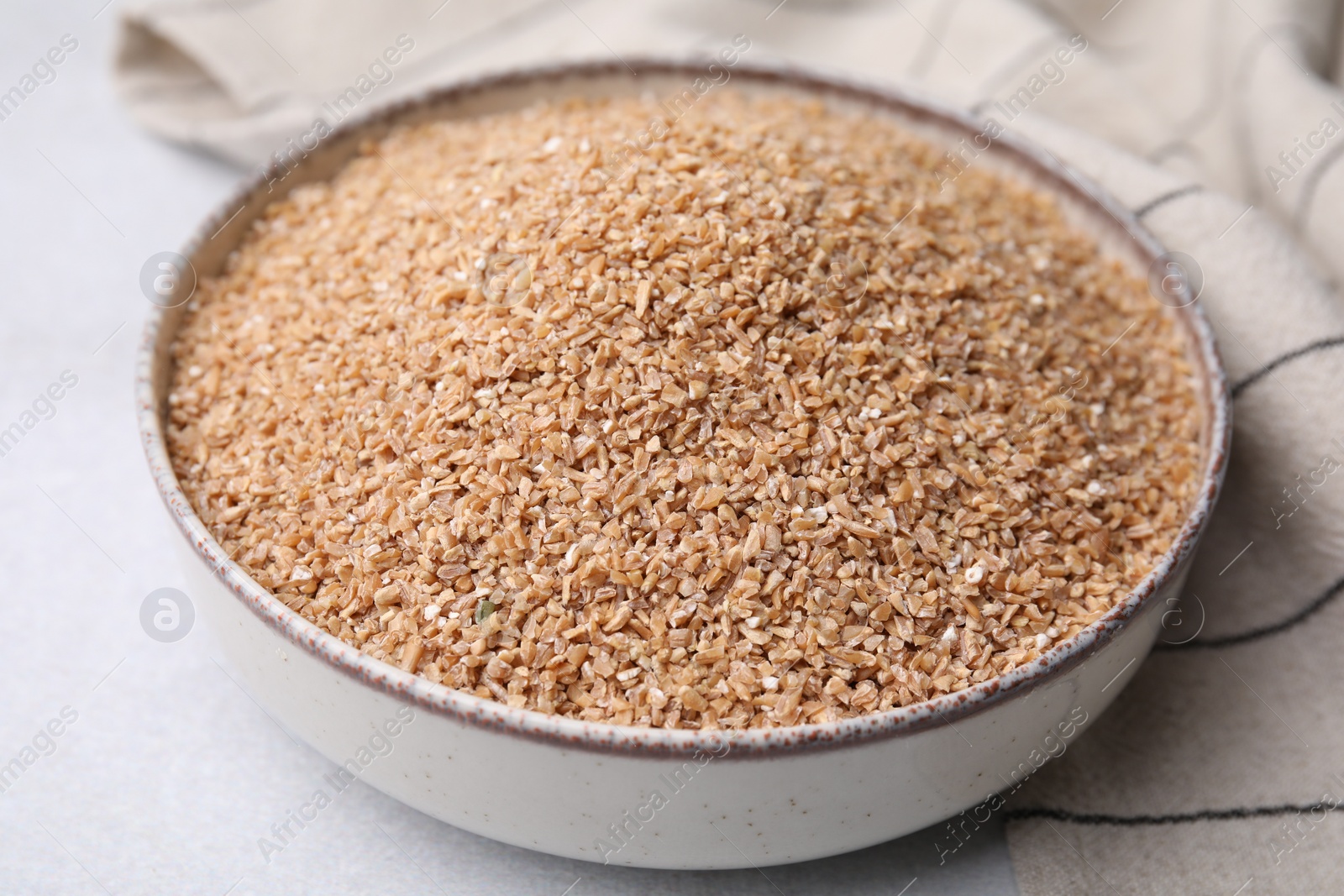 Photo of Dry wheat groats in bowl on light table, closeup