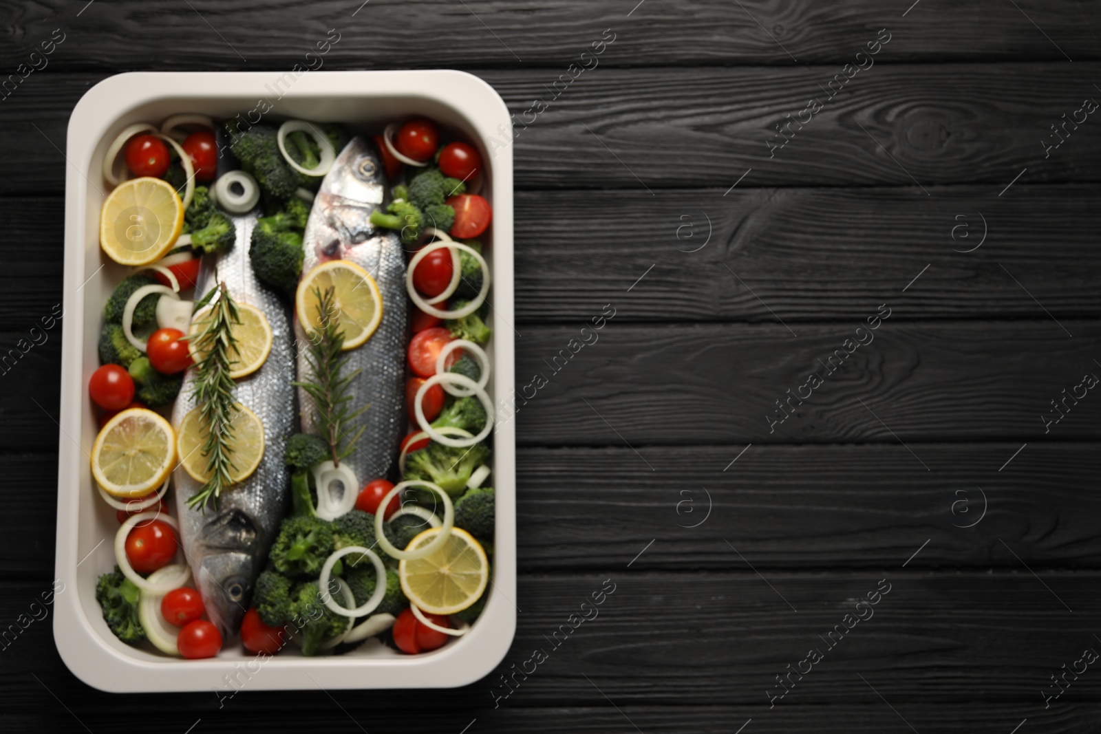 Photo of Raw fish with vegetables and lemon in baking dish on black wooden table, top view. Space for text