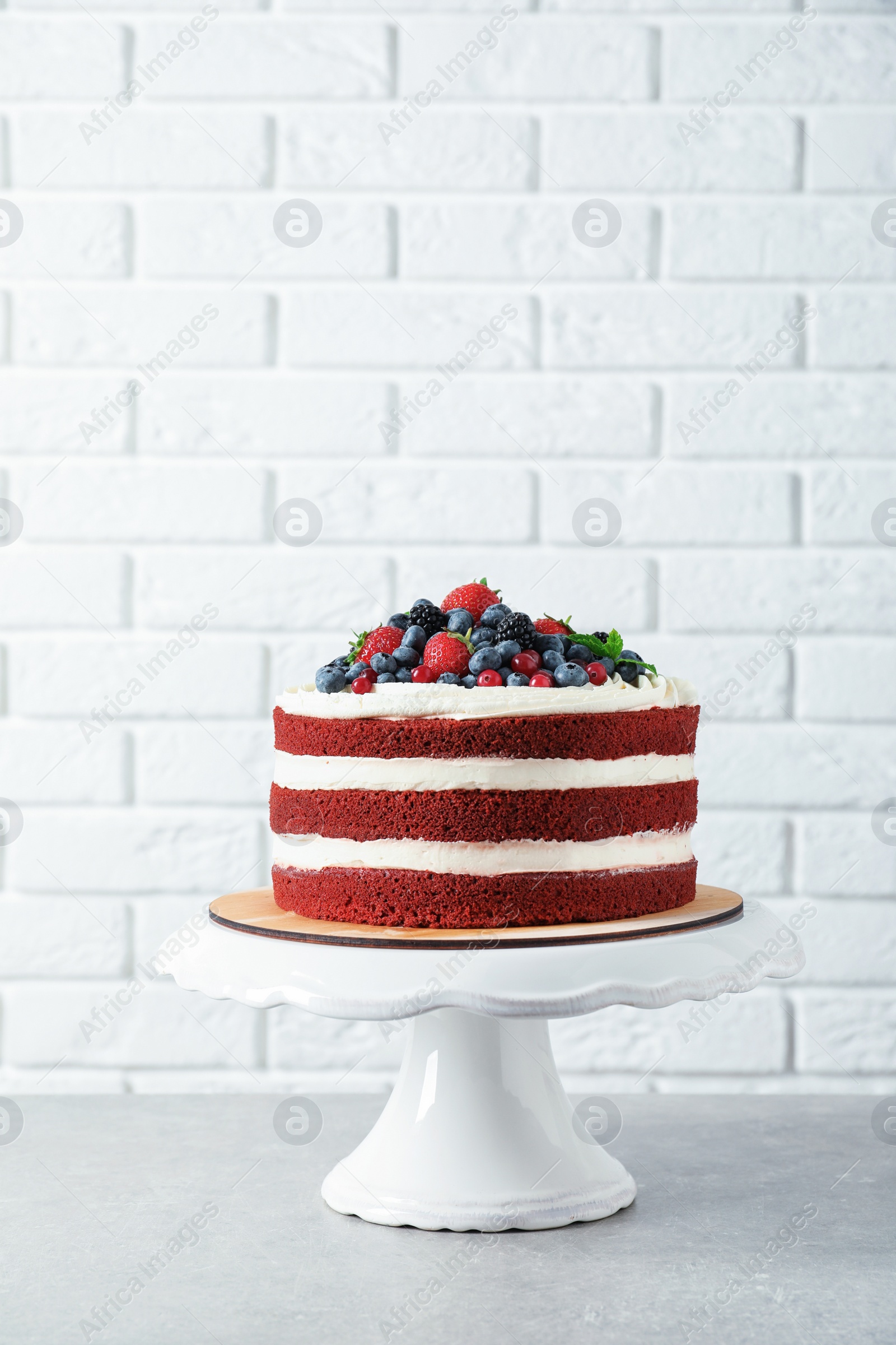 Photo of Stand with delicious homemade red velvet cake near brick wall