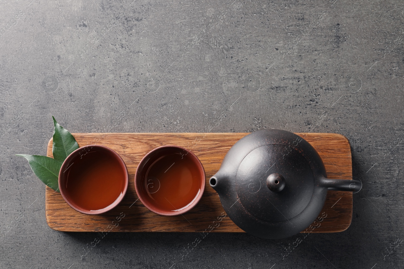 Photo of Board with cups and teapot of freshly brewed oolong on grey background, top view with space for text