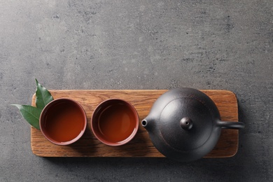 Photo of Board with cups and teapot of freshly brewed oolong on grey background, top view with space for text