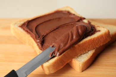 Photo of Tasty toast with chocolate paste and knife on wooden board, closeup