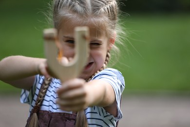 Photo of Little girl playing with slingshot outdoors, selective focus. Space for text