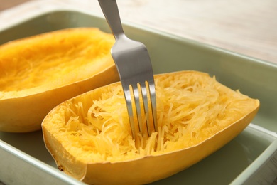 Photo of Scraping flesh of cooked spaghetti squash with fork in baking dish