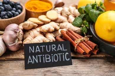 Photo of Different fresh products and card with phrase Natural Antibiotic on wooden table, closeup