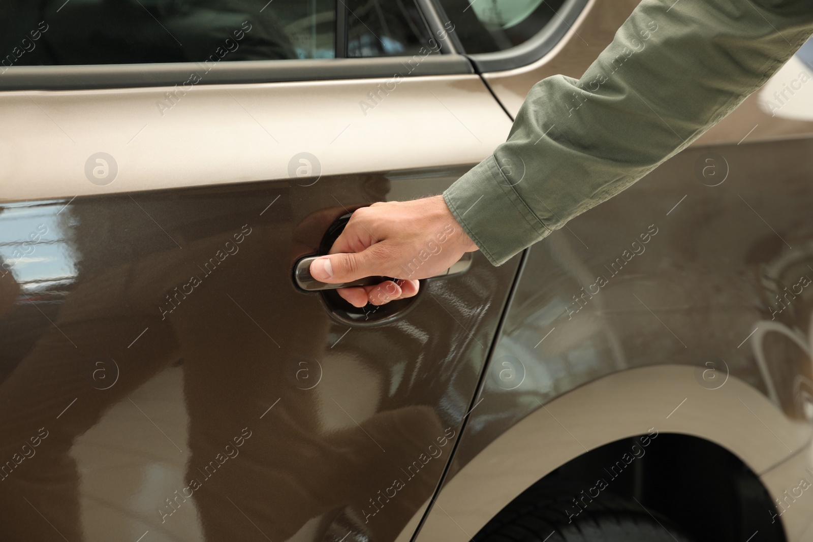 Photo of Young man opening car door in modern auto dealership, closeup