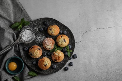 Photo of Delicious muffins with powdered sugar, blueberries and mint on light grey table, flat lay. Space for text