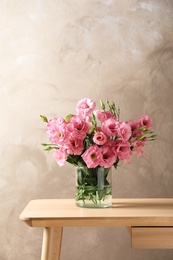 Photo of Vase with beautiful Eustoma flowers on table against color background