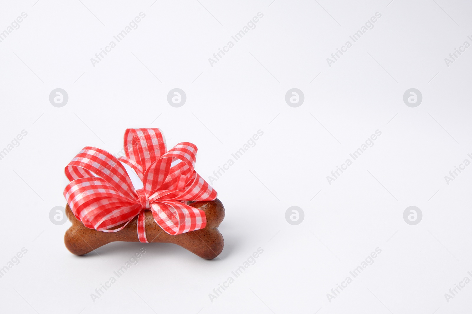 Photo of Bone shaped dog cookie with red bow on white background, space for text
