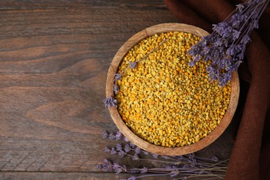 Photo of Fresh bee pollen granules in bowl and lavender on wooden table, top view. Space for text