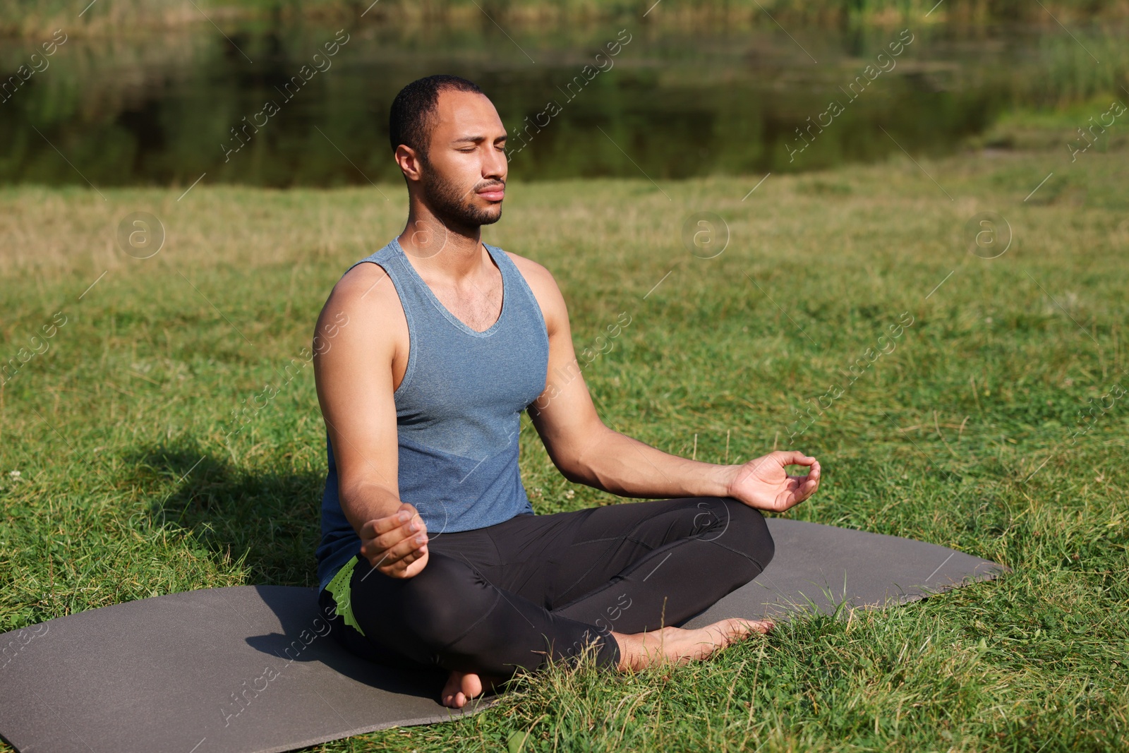 Photo of Man practicing yoga on mat outdoors. Lotus pose