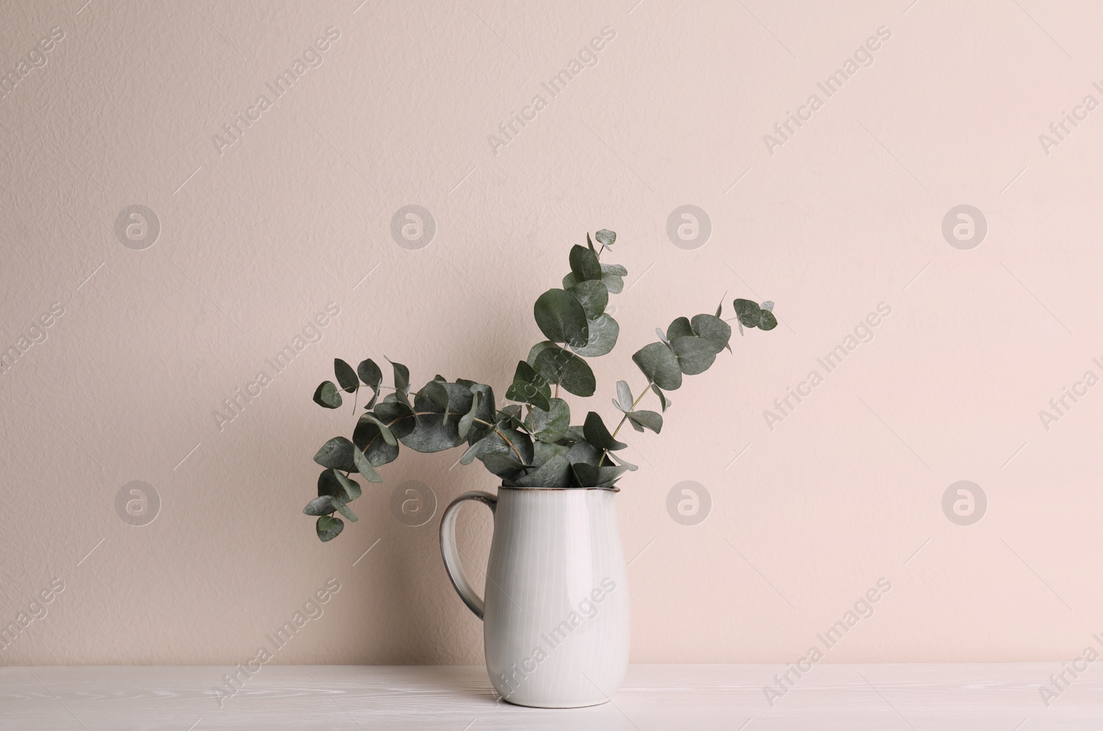 Photo of Vase with beautiful eucalyptus branches on white wooden table near beige wall