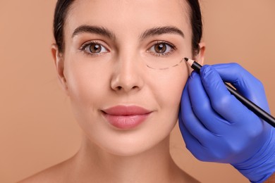 Photo of Doctor drawing marks on woman's face for cosmetic surgery operation against beige background, closeup
