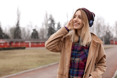 Photo of Young woman with headphones listening to music outdoors. Space for text