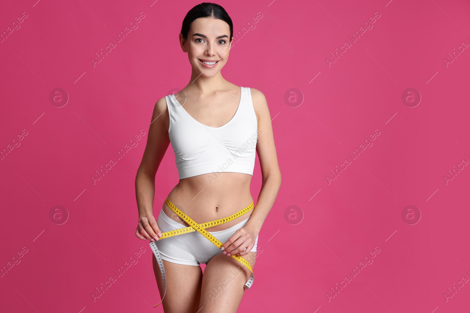 Photo of Young woman measuring waist with tape on pink background. Space for text