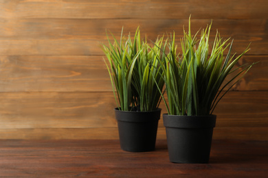 Photo of Artificial plants in dark flower pots on wooden table