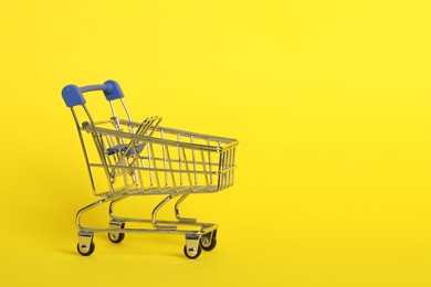 Photo of Small metal shopping cart on yellow background. Space for text