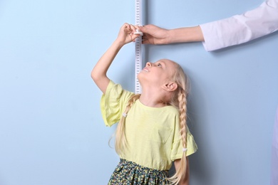 Photo of Doctor measuring little girl's height on light background