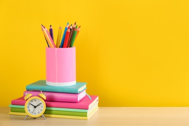 Photo of Different school stationery and alarm clock on table against yellow background, space for text. Back to school