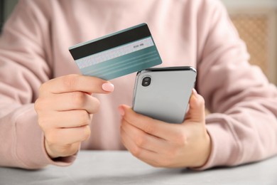 Online payment. Woman using credit card and smartphone at light grey table indoors, closeup