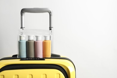 Photo of Cosmetic travel kit in plastic bag on suitcase against light background, space for text