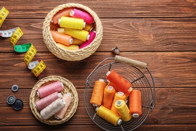 Color sewing threads and measuring tape on wooden background, flat lay