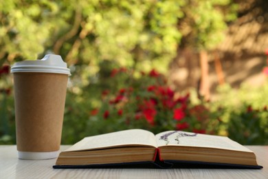 Photo of Open book with paper cup of coffee and dried flowers on wooden table in garden