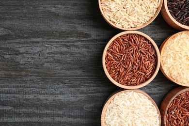 Flat lay composition with brown and other types of rice in bowls on wooden background. Space for text