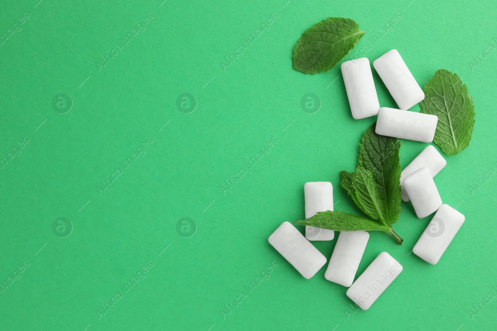 Photo of Tasty white chewing gums and mint leaves on green background, flat lay. Space for text