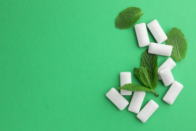 Photo of Tasty white chewing gums and mint leaves on green background, flat lay. Space for text