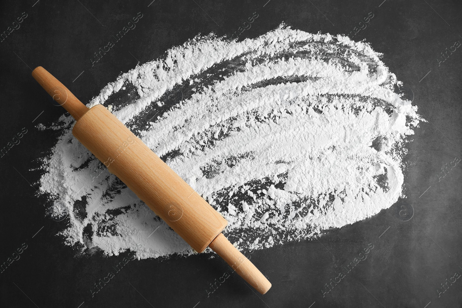 Photo of Scattered flour and rolling pin on black table, top view