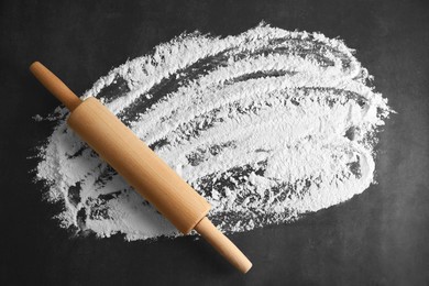 Photo of Scattered flour and rolling pin on black table, top view