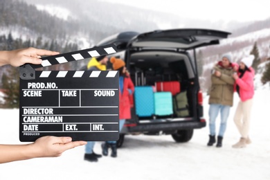Image of Assistant holding clapperboard and people near car on snowy road, closeup. Cinema production 