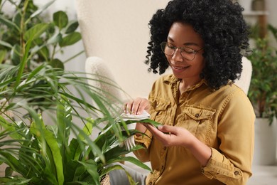 Happy woman wiping beautiful houseplant leaves indoors