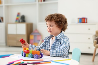 Photo of Cute little boy playing with toy cars at white table in kindergarten