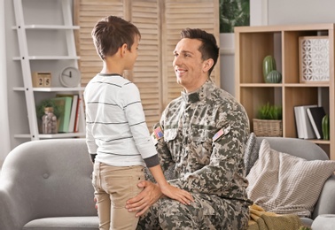 Young man in military uniform with his little son at home