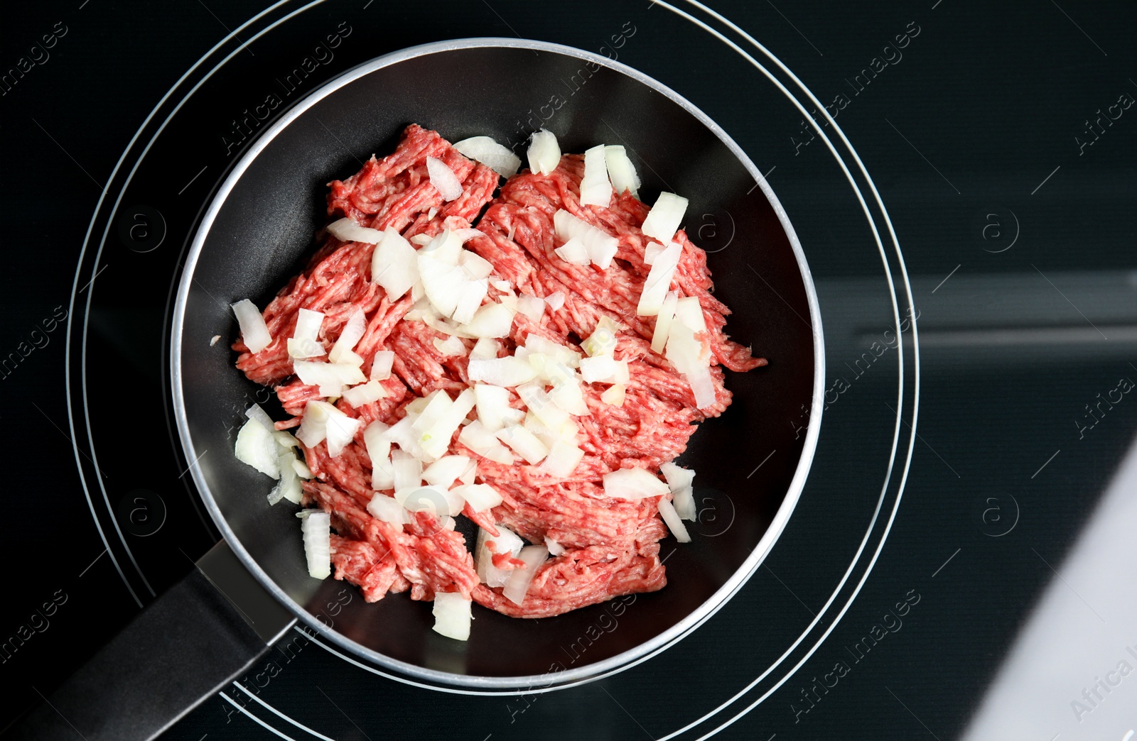 Photo of Frying pan with raw minced meat and chopped onion on induction stove, top view